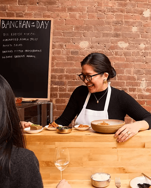 Chef Sunny Lee at Sunn’s NYC in Chinatown serving fresh banchan to guests at the counter.